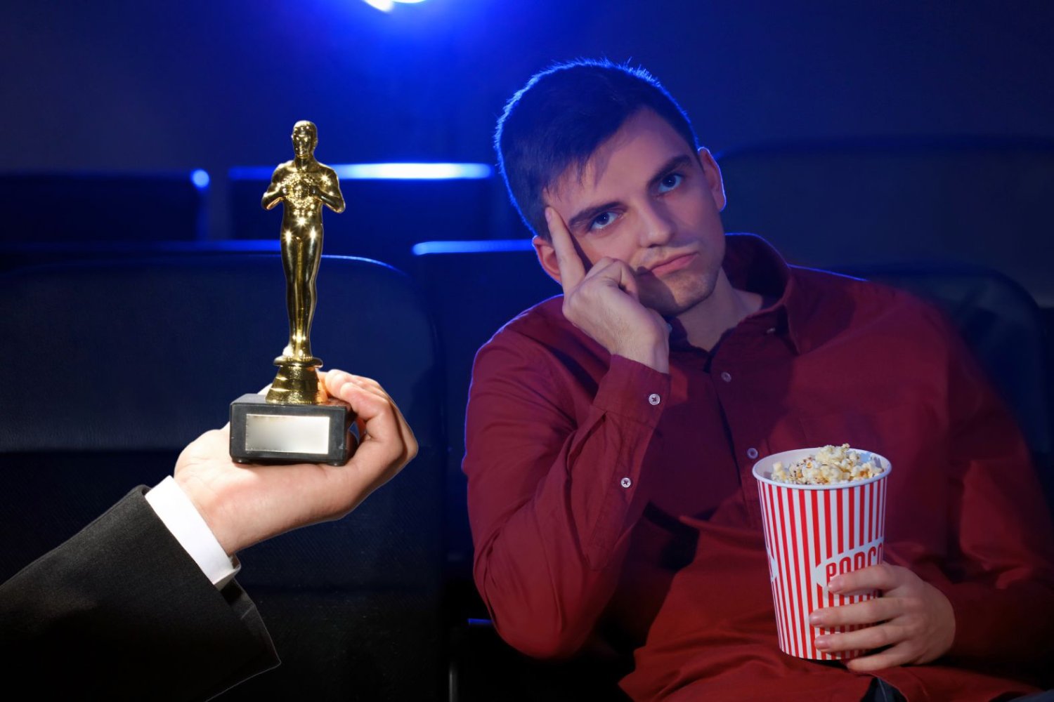 Na zdjęciu widzimy znudzonego mężczyznę siedzącego na fotelu kinowym.