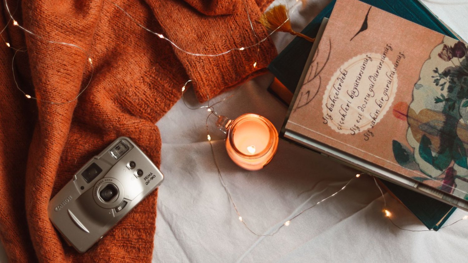 Sweter, świeczka, książka i aparat fotograficzny na kocu