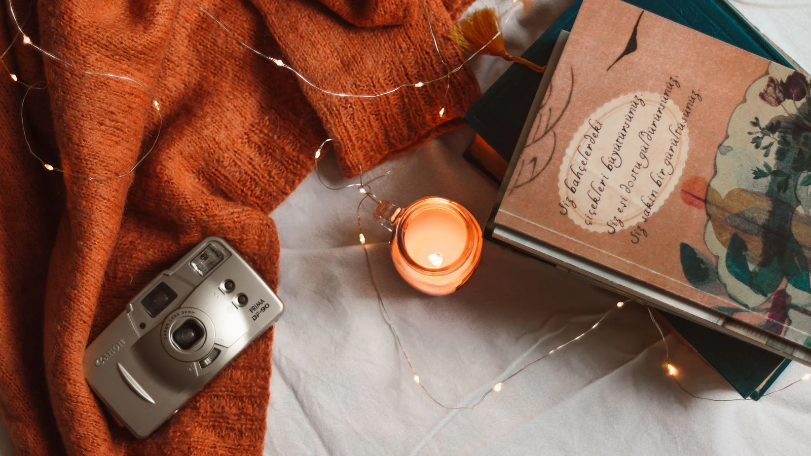 Sweter, świeczka, książka i aparat fotograficzny na kocu